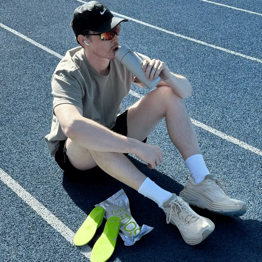 Runner resting on a track with SOLE5 orthotic insoles beside a water bottle
