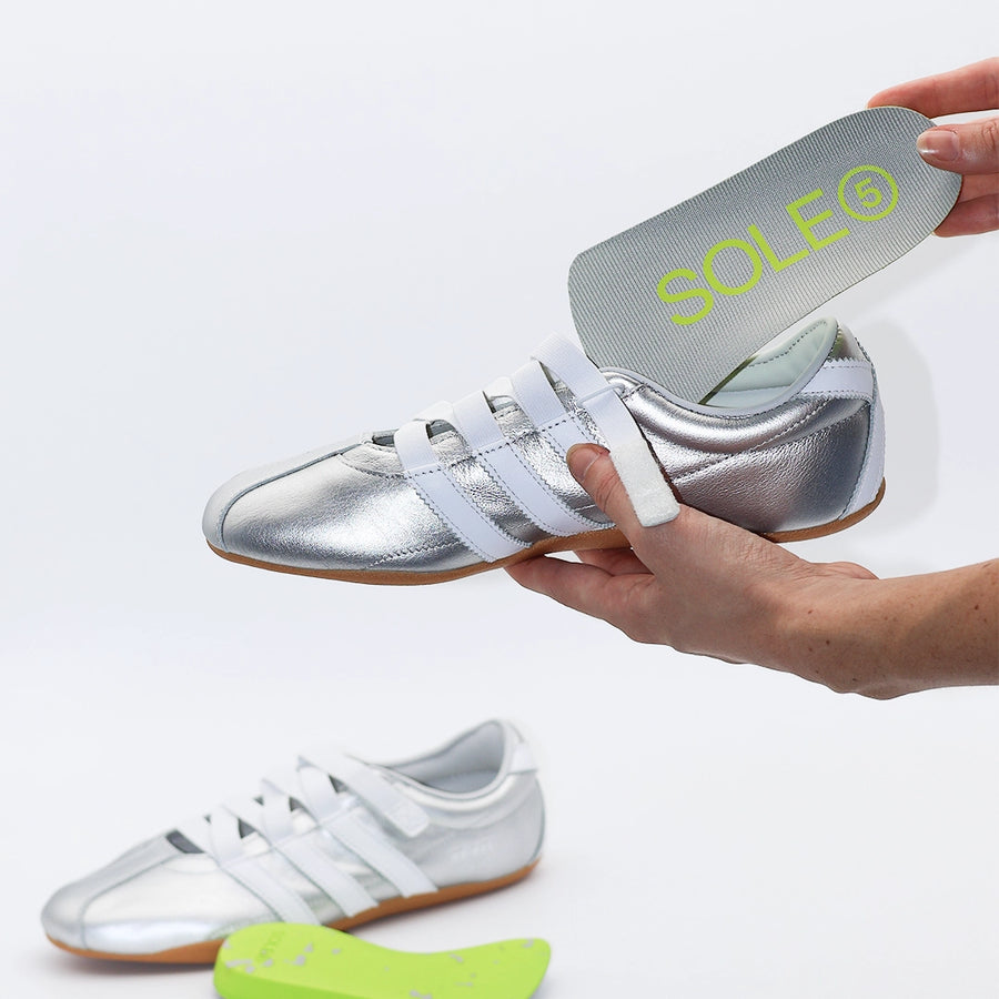 A Half Length SOLE5 Orthotic Insole being placed inside a silver coloured casual shoe
