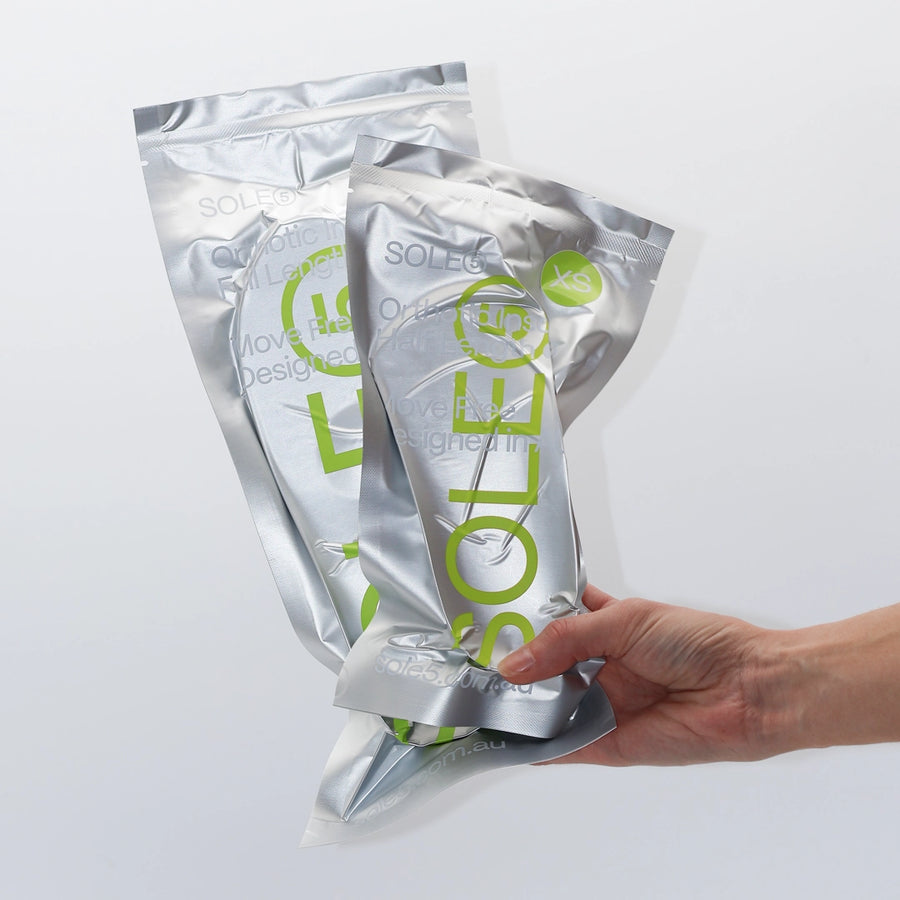 A hand holding the silver vacuumed sealed packaging for both of SOLE5's Full Length & Half Length Orthotic Insoles