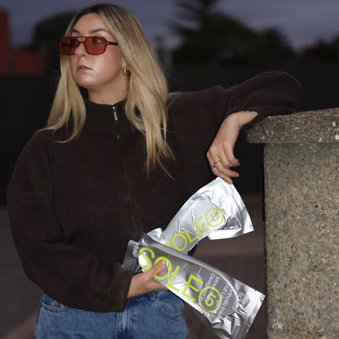 Person holding two SOLE5 packages, standing against a dark background.