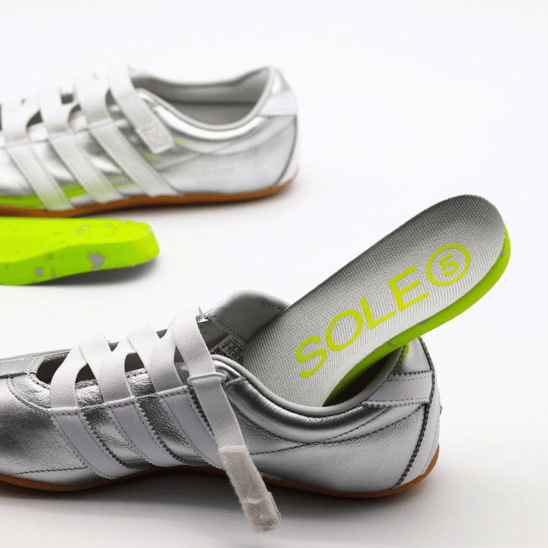 SOLE5 green half length orthotic insole going in a Silver sneaker on a white background