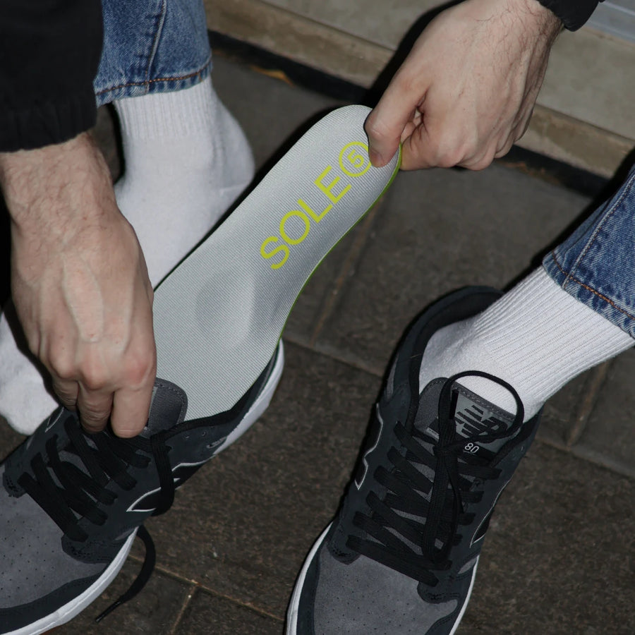 Person placing a SOLE5 Full Length Orthotic Insole inside their black sneakers