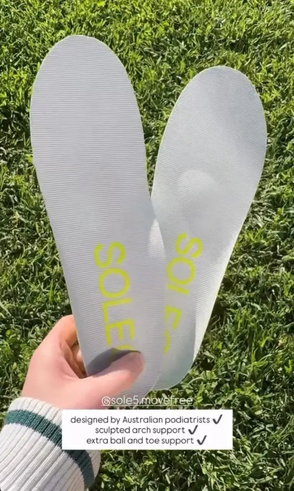 A hand holds a pair of SOLE5 Full Length orthotic insoles over a green grass background. A text overlay at the bottom lists features like 'sculpted arch support' and 'extra ball and toe support'.