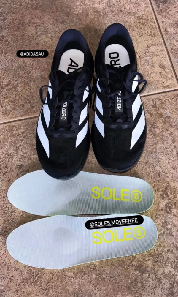 A pair of black Adidas Adizero running shoes, displayed above a pair of SOLE5 Full Length orthotic insoles, set on a brown tiled floor.