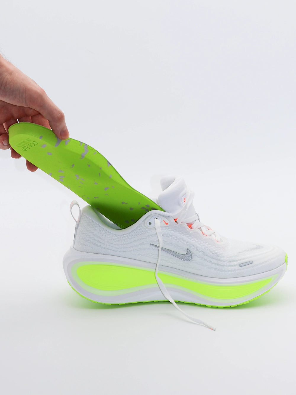 White and green running shoe with a hand placing a SOLE5 Full Length Orthotic Insole inside it