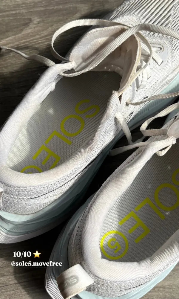 A pair of white sneakers with SOLE5 orthotic insoles inside them. Shown on a dark wood floor.